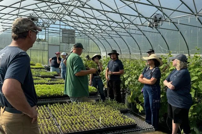 A group of people standing in a green house getting instructions from a man in a green shirt