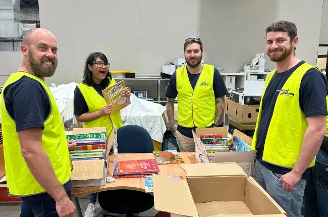 Four people in safety vests smiling at the camera with books in front of them