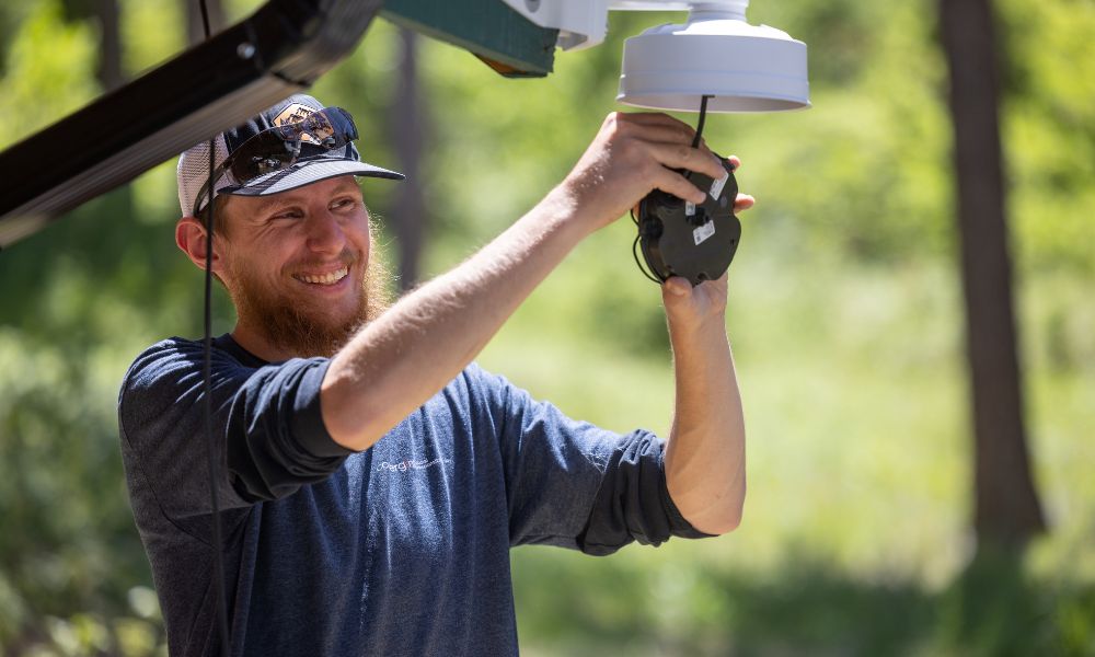 A man in a blue shirt and a hat on working on a security camera